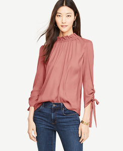 Ruched sleeve ties make our shirred mock neck distinctly feminine - and extra pretty. Shirred ruffle mock neck with back self ties. 3/4 sleeves with tunneled self ties. 23 3/4 long.