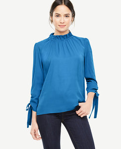 Ruched sleeve ties make our shirred mock neck distinctly feminine - and extra pretty. Shirred ruffle mock neck with back self ties. 3/4 sleeves with tunneled self ties. 23 3/4 long.